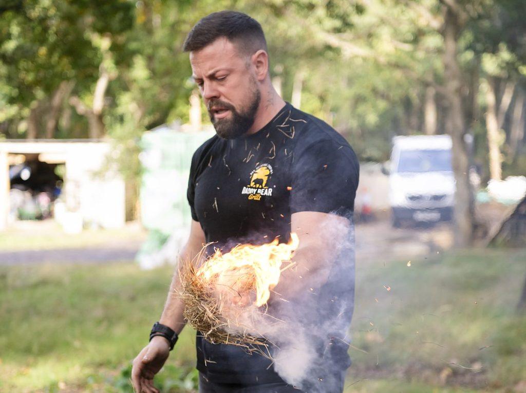 Wayne Smith lighting a straw bundle by hand over a fire bowl at a fire lighting workshop