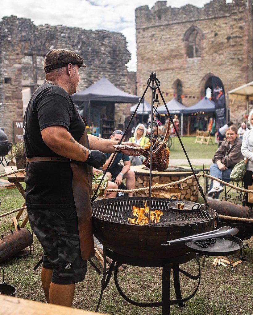 Wayne Smith cooking a tomahawk steak over a Kadai fire bowl at a live fire festival